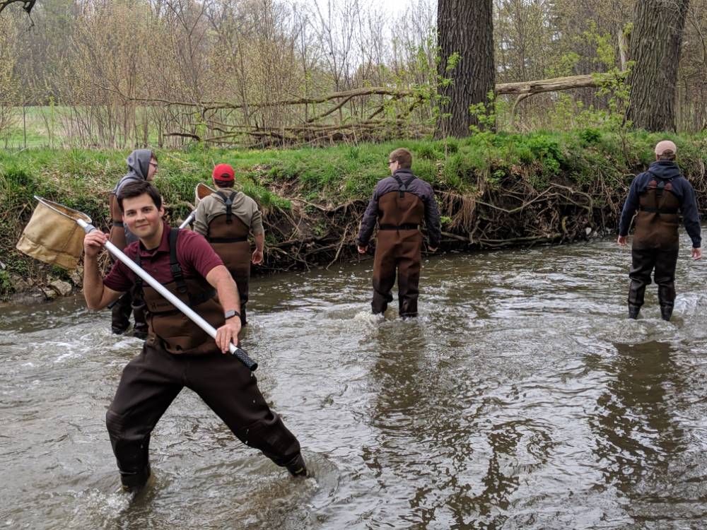A student in waders holds a net on his shoulder